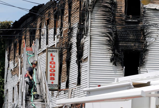 A firefighter works on a ladder outside a burned three-story apartment and business building in Lowell, Mass., Thursday, July 10, 2014, where officials said four adults and three children died in a fast-moving pre-dawn fire.