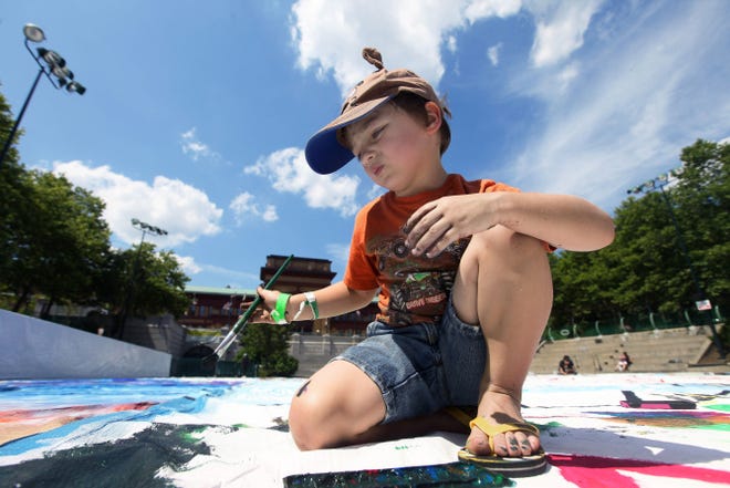 Tristan Paulo, 4, of West Warwick, looks over his work as he contributes to a public mural about Providence neighborhoods that filled the Bank of America rink, in Providence, Saturday afternoon.