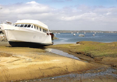 The large white yacht Guest List, with no engine or rudder, sits in the salt marshes near the Hampton Marina.