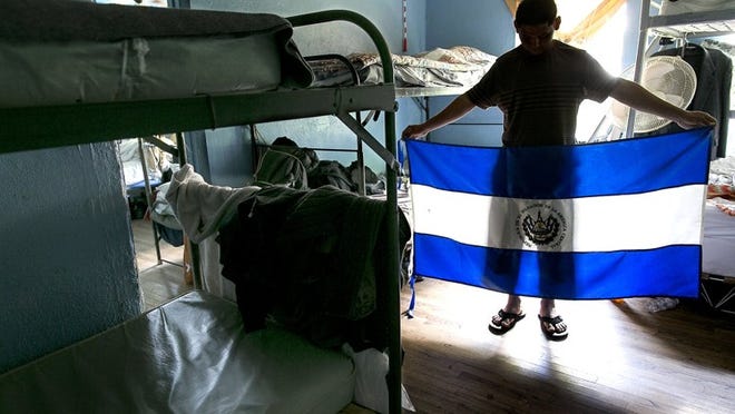 José, 18, unfurls a flag from his home country of El Salvador in his room at an Austin shelter, Casa Marianella. He asked that his last name be withheld because he fears that the gang members who tried to recruit him will harm the family he left behind.