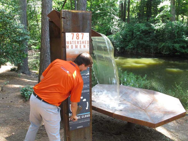 Clemson University student William Craig turns a crank that fills part of a sculpture designed by his fellow architecture students to represent the flood that destroyed the South Carolina Botanical Garden on Wednesday, July 23, 2014, in Clemson, S.C. Clemson students helped rebuild the garden after a July 2013 flood did $225,000 in damage and swept away thousands of plant species. (AP Photo/Jeffrey Collins)