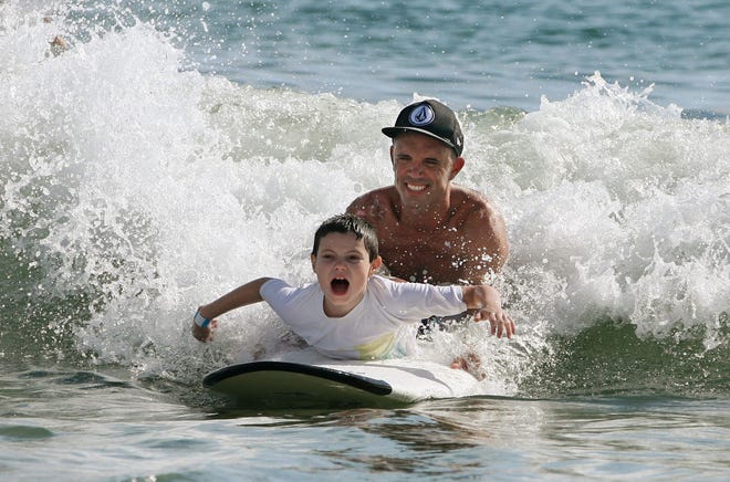 John West, 8, of Port Orange, rides the waves in Ponce Inlet with the help of Timothy Shirley during Saturday’s Surfers for Autism event. For more photos, see PAGE 2B or see the gallery at news-journalonline.com.