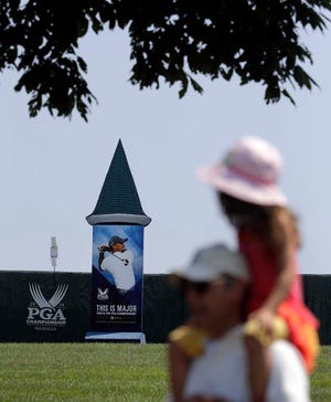 Golf fan Nevin Baker carries his daughter, Sophia, 4, on his shoulders as they walk past a photo of Tiger Woods at the PGA Championship golf tournament at Valhalla Golf Club Monday, Aug. 4, 2014, in Louisville, Ky. The tournament is set to begin on Thursday. (AP Photo/Jeff Roberson)