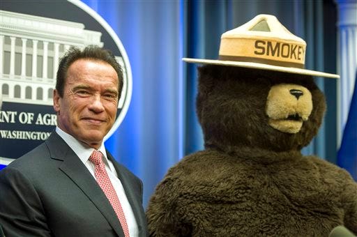 FILE - This Oct. 30, 2013 file photo shows former California Governor Arnold Schwarzenegger posing with Smokey Bear after the U.S. Forest Service named him their third honorary Forest Ranger for his leadership on climate change during a ceremony at the Department of Agriculture.in Washington. Smokey Bear is turning 70 on Saturday Aug. 9, 2014 _ but don’t bring any candles to the party, please.