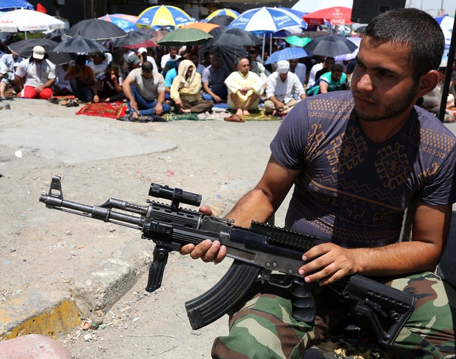 A Shiite fighter strands guard next to followers of Shiite cleric Muqtada al-Sadr attending open-air Friday prayers in the Shiite stronghold of Sadr City, Baghdad, Iraq, Friday, Aug. 8, 2014. The U.S. began airstrikes on Islamic militants in Iraq on Friday, the Pentagon said.