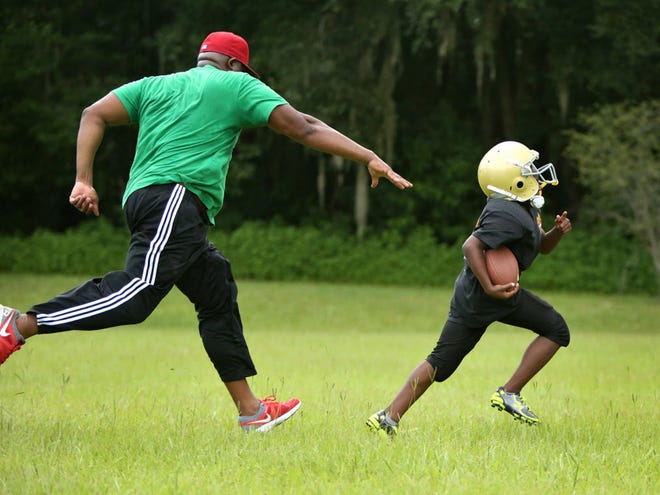 Stephen Morrison, 9, runs away from the outstretched hand of his cousin Tony Caffie as they practice football drills in preparation of the start of the Boys and Girls Club football season, at Squirrel Ridge Park in Gainesville Aug. 10, 2014.