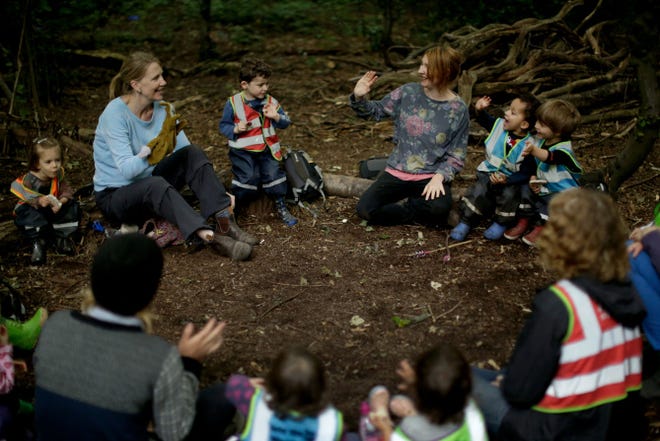 Founder Emma Shaw, top left, leads a game with a hand puppet. A circle of logs provides a place to gather for snacks, stories and songs.