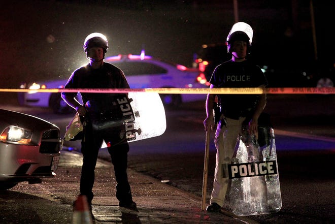 Police wearing riot gear stand at a post as they wait for a crowd to disperse Monday, Aug. 11, 2014, in Ferguson, Mo.