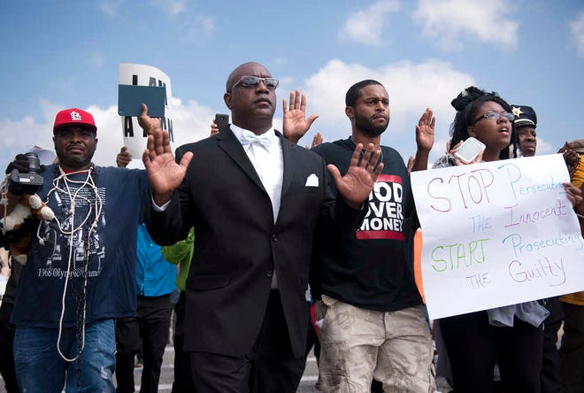Protestors march along Florissant Road in downtown Ferguson, Mo. Monday, Aug. 11, 2014. The group marched along the closed street, rallying in front of the town's police headquarters to protest the shooting of 18-year-old Michael Brown by Ferguson police officers on Saturday night. (AP Photo/Sid Hastings)