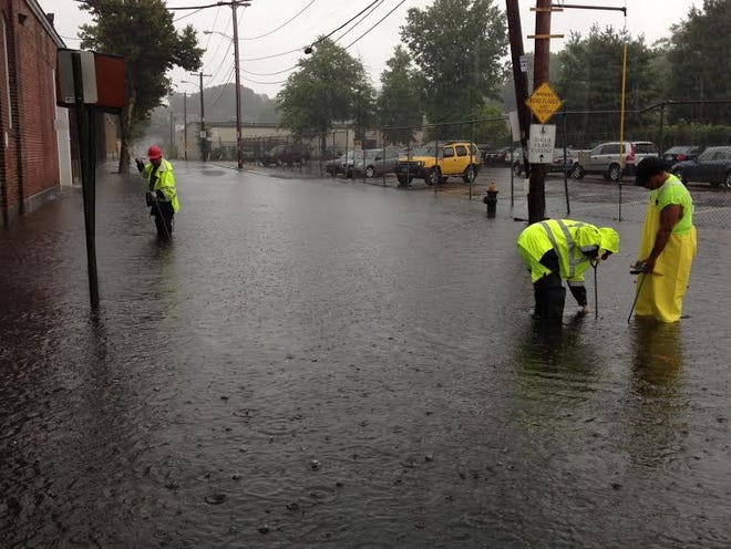 Providence DPW workers struggle to unplug storm drains at corner of Admiral and Whipple, where the water was flooding part of the intersection.