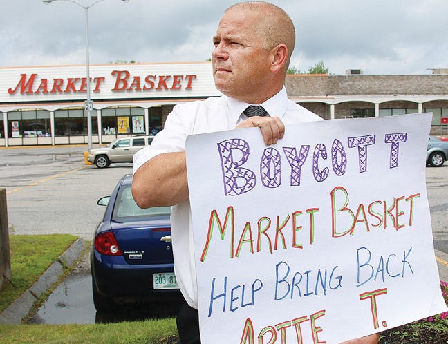 Mark Owens, store manager at the Market Basket in Stratham holds a sign in front of the store recently during his break.