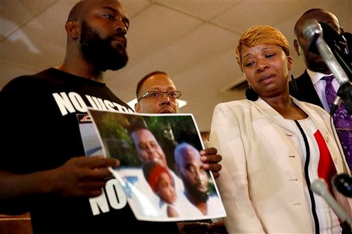 Lesley McSpadden, right, the mother of 18-year-old Michael Brown, watches as Brown's father, Michael Brown Sr., holds up a family picture of himself, his son, top left in photo, and a young child during a news conference Monday, Aug. 11, 2014, in Ferguson, Mo. Michael Brown, 18, was shot and killed in a confrontation with police in the St. Louis suburb of Ferguson, Mo, on Saturday, Aug. 9, 2014. (AP Photo/Jeff Roberson)