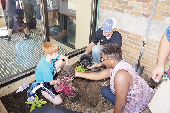 Boys & Girls Club members Nick Phillips, 12, and Kamiah Bridges, 16, work with Lowe’s racing team member Jesse Saunders to work on the landscaping project Thursday at the club.