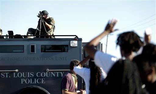 A member of the St. Louis County Police Department points his weapon in the direction of a group of protesters in Ferguson, Mo. on Wednesday, Aug. 13, 2014. On Saturday, Aug. 9, 2014, a white police officer fatally shot Michael Brown, an unarmed black teenager, in the St. Louis suburb. (AP Photo/Jeff Roberson)