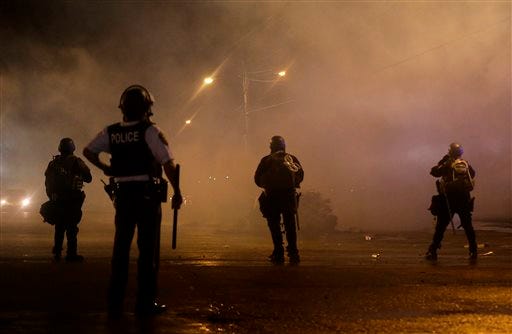 A law enforcement officer watches Sunday, Aug. 17, 2014, as tear gas is fired to disperse a crowd protesting the shooting of teenager Michael Brown last Saturday in Ferguson, Mo. Brown's shooting in the middle of a street following a suspected robbery of a box of cigars from a nearby market has sparked a week of protests, riots and looting in the St. Louis suburb.