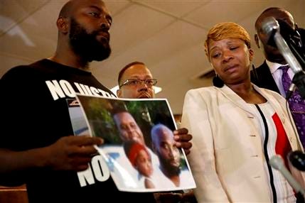 Lesley McSpadden, right, the mother of 18-year-old Michael Brown, watches as Brown's father, Michael Brown Sr., holds up a family picture of himself, his son, top left in photo, and a young child during a news conference Monday, Aug. 11, 2014, in Ferguson, Mo. Michael Brown, 18, was shot and killed in a confrontation with police in the St. Louis suburb of Ferguson, Mo, on Saturday, Aug. 9, 2014. Autopsy results have not yet determined whether Brown had his hand up when he was shot as witnesses contend.