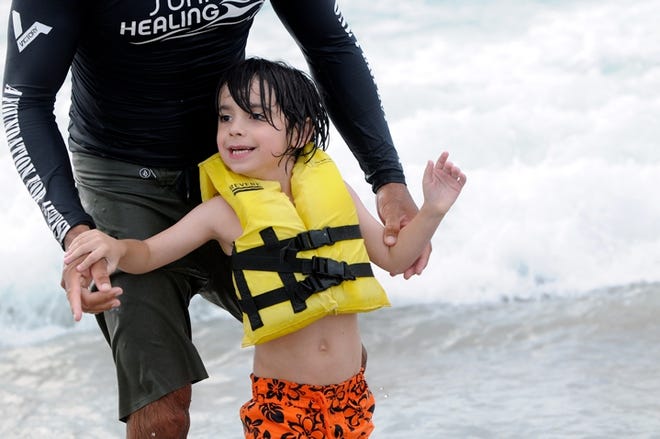 Kamu Davis helps Manuel Armendariz, 7, catch a wave Monday, Aug. 18, 2014, at Wrightsville Beach during the annual Surfers Healing event for children with autism. Hundreds of people made their way to the beach to watch and cheer on the camp that was founded by Israel and Danielle Paskowitz.