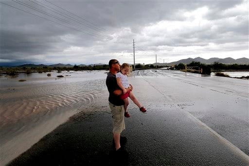 Josh Groves, and his daughter Abagayle Groves, 3, wait to cross the road as flash flood waters overrun Skunk Creek through the Sonoran Desert, Tuesday, Aug. 19, 2014, in northwestern Phoenix. Flooding from heavy rain in the Phoenix area has forced authorities to close several major roads, including a portion of Interstate 17 about 25 miles north of the city. (AP Photo/Matt York)