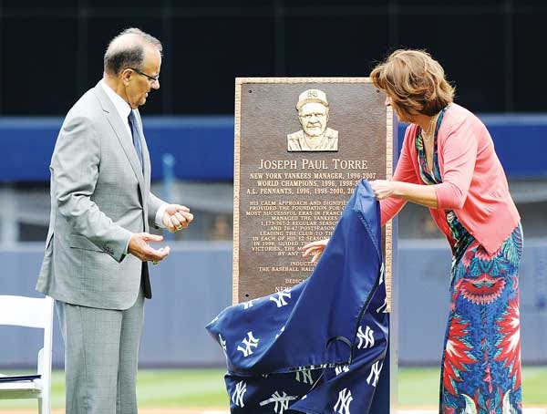 AP Photo/Bill Kostroun — Former New York Yankees manager Joe Torre, left, reacts as his wife, Ali, uncovers a replica of his plaque that will hang in Monument Park as the Yankees retired his number before their game Saturday against the Chicago White Sox.