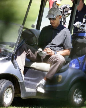 President Barack Obama operates an electronic device while golfing at Farm Neck Golf Club, in Oak Bluffs, Mass., on the island of Martha's Vineyard, Thursday, Aug. 21, 2014. Obama is vacationing on the island. (AP Photo/Steven Senne)
