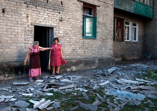 In this photo taken Wednesday, Aug. 27, 2014, local residents stand near the building where they live after a shelling in Donetsk, eastern Ukraine. Two columns of Russian tanks and military vehicles fired Grad missiles at a border post in southeastern Ukraine, then rolled into the country Thursday as Ukraine's overmatched border guards fled, a top Ukrainian official said.
