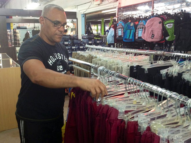 In this, Saturday, Aug. 23, 2014 photo, Roberto Salgado, 44, looks through a row of burgundy-red pants similar to the ones used by Cuban primary school students, at Nooo Que Barato in Hialeah, Fla.