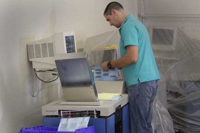 Matt Hozempa, of the R.I. Board of Elections, puts mail ballots through the counting machine at the board's offices in Providence.