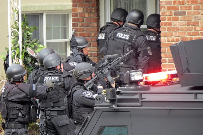 FILE - In this April 22, 2014, file phot, Nassau County police officers enter a home in Long Beach, N.Y., in search of an armed killer, based on a phone call that turned out to be a hoax. Authorities say the dangerous and costly prank known as "swatting", is becoming increasingly popular among people who play combat games over live video feeds while thousands of people watch. Authorities estimated they spent $100,000 to send more than 60 officers to the Long Beach, Long Island swatting hoax.