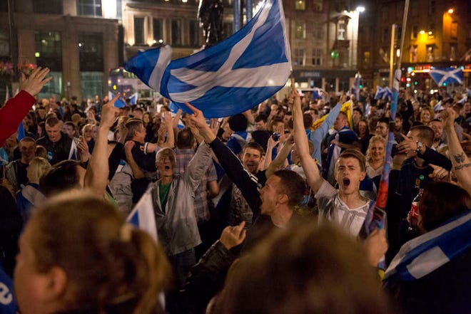Supporters of the Yes campaign in the Scottish independence referendum cheer with Scottish Saltire flags as they await the result after the polls closed, in George Square, Glasgow, Scotland, late Thursday, Sept. 18, 2014. From the capital of Edinburgh to the far-flung Shetland Islands, Scots embraced a historic moment - and the rest of the United Kingdom held its breath - after voters turned out in unprecedented numbers for an independence referendum that could end the country's 307-year union with England. (AP Photo/Matt Dunham)