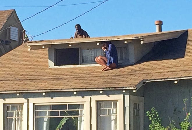 CORRECTS NAME FROM LAURA RIVERA TO MELORA RIVERA - In this Wednesday, Sept. 24, 2014 photo, Melora Rivera, who fled her house through an attic window to escape an intruder, seen on the roof behind her, waits for help after an early-morning break in at her house in the Venice neighborhood of Los Angeles. The intruder, later identified as Christian Hicks, was arrested by Los Angeles police officers and is being held for investigation of burglary. (AP Photo/Venice311.org, Alex Thompson) MANDATORY CREDIT