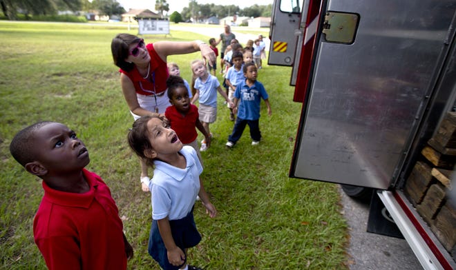 Marion Charter School kindergarteners Terrence Isaac (far left), Sarielys Morales Santiago (middle) and Cheyenne Bowen(far right) look on as their teacher Beth Dillingham points out different features of a fire truck in Ocala on Thursday.