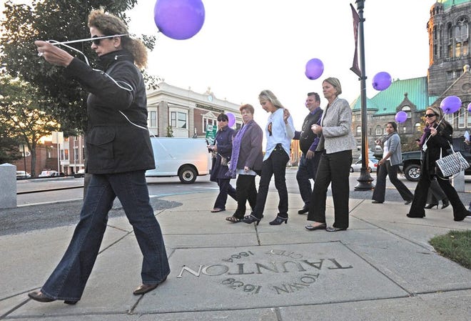 Annemarie Matulis, organizer of the 12th annual Candlelight Vigil Against Domestic Violence, at center wearing a purple scarf, walks with the group around the Taunton Green on Monday night.