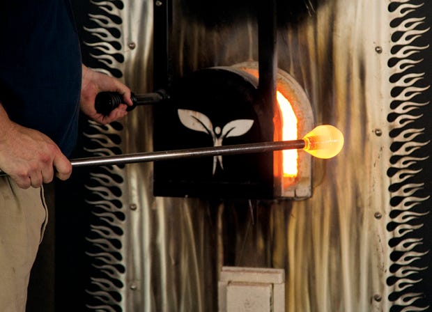 Stepanski places the red-hot end of a pipe in a large furnace and gently spins it to collect molten glass on the end.