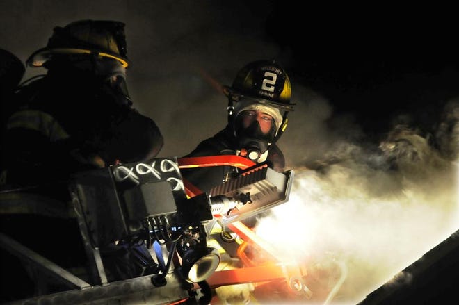 Two firefighters surrounded by smoke work on opening up a section of the roof at 8 First St., Manchaug, Monday night.