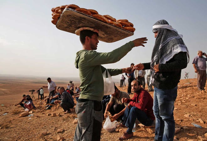 A vendor sells bread on a hilltop on the outskirts of Suruc, at the Turkey-Syria border, as people gather to watch fighting between Syrian Kurds and the militants of Islamic State group in Kobani, Syria, on Monday, Oct. 13, 2014. Kobani, also known as Ayn Arab, and its surrounding areas, has been under assault by extremists of the Islamic State group since mid-September and is being defended by Kurdish fighters.