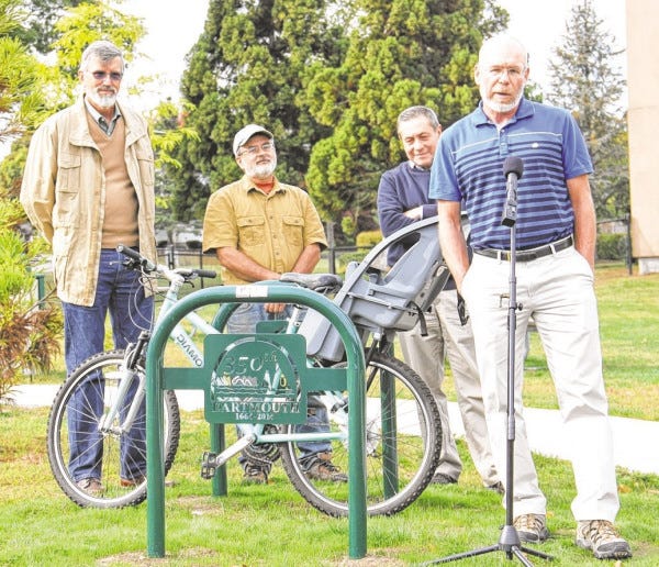 Collectively smiling at another sign of progress for the Dartmouth Pathways Committee, a new grant-funded bike rack just installed at Southworth Library, are committee members (l-r) Gerard Koot, Mike Labossiere, and Gus Raposo, listening to chair Alan Heureux at a public unveiling between Dartmouth Community Park and Southworth Library.