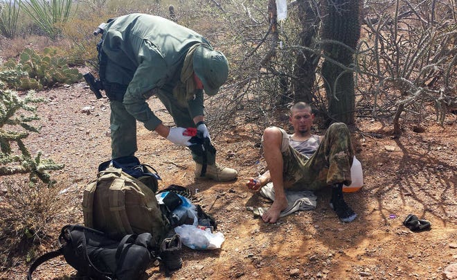 In this June 25, 2014 photo, an unidentified U.S. Border Patrol agent, left, helps an immigrant, including setting up intravenous fluid replacement for dehydration, near Sells, Ariz. The number of migrants who died or needed rescue while crossing the desert from Mexico into Arizona has dropped significantly this year. (AP Photo/Astrid Galvan)