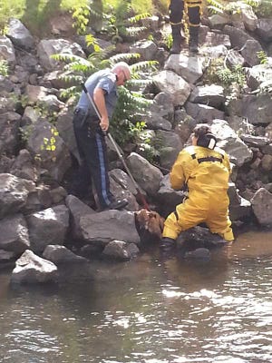 Submitted photo - Stanhope Police Sgt. Charles Zweigle and a member of the Stanhope Borough Fire Department work to rescue a dog that had been nestled in the rocks lining the side of the Musconetcong River on Friday afternoon.