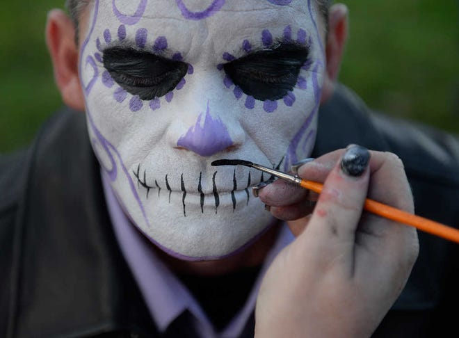 Brittney Lohmiller / Savannah Morning News - Alyson Harris paints a mustache on Wayne Crews during the 7th annual Zombie Walk. Crews and his wife painted their faces to look like Day of the Dead candy skeletons.
