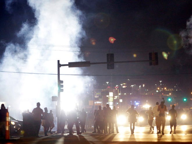 FILE - In this Monday, Aug. 18, 2014 file photo, people stand near a cloud of tear gas in Ferguson, Mo. during protests for the Aug. 9 shooting of unarmed black 18-year-old Michael Brown by a white police officer. The U.S. government agreed to a police request to shut down several miles of airspace surrounding Ferguson, even though authorities said their purpose was to keep media helicopters away during protests in August, according to recordings of air traffic control conversations obtained by The Associated Press.