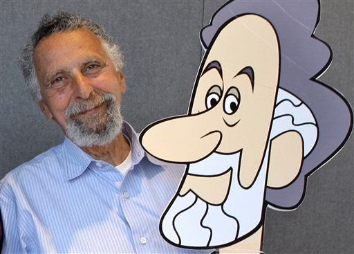 In this June 19, 2008 photo, Tom Magliozzi, co-host with his brother Ray of National Public Radio's "Car Talk" show, poses with a caricature of himself in Cambridge, Mass. NPR says Magliozzi died Monday, Nov. 3, 2014 of complications from Alzheimer's disease. He was 77. (AP Photo/Charles Krupa)