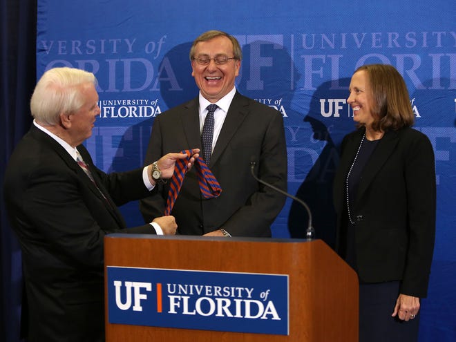 In this Oct. 15, 2014 file photo, University of Florida President-elect Kent Fuchs is presented with an orange and blue tie by UF Board of Trustees Chair Steven Scott at Emerson. At right is Fuchs' wife, Linda.