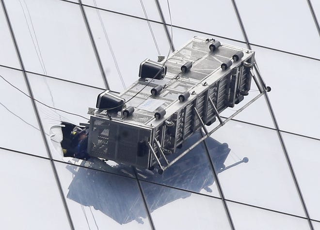 A firefighter reaches through a cut-out window into a dangling work basket to rescue two workers from the 60th floor of 1 World Trade in New York, Wednesday, Nov. 12, 2014. The two window washers were trapped for more than an hour. The dramatic rescue occurred on the south side of the 1,776-foot, 104-story building, where the open-topped platform hung at about a 45-degree angle and swayed slightly in the wind.