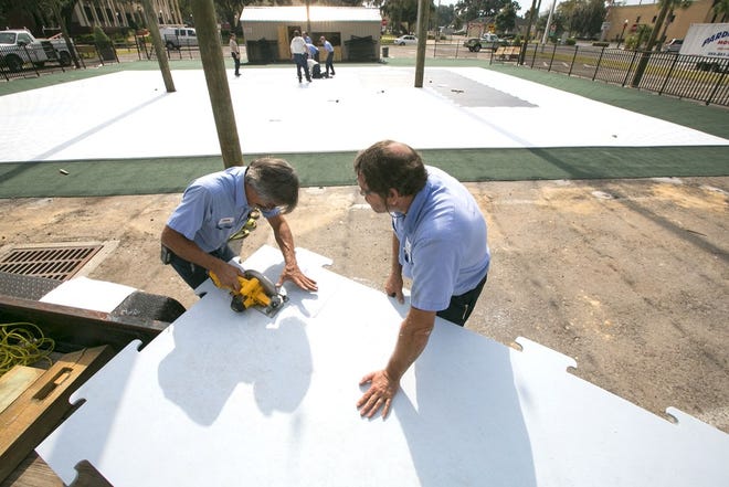 City workers Edwin Solero, left, and Les Ackerman trim a sheet of synthetic ice rink near Citizens' Circle in downtown Ocala.