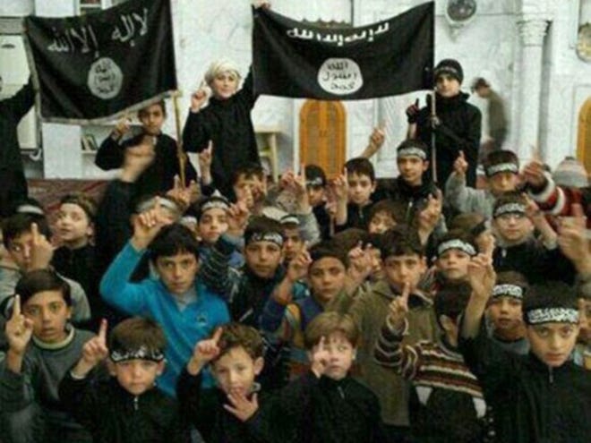 In this undated image posted online and made available on Thursday, Nov. 20, 2014, by Raqqa Is Being Slaughtered Silently, an anti-Islamic State group organization, children pose with Islamic State group flags in Raqqa, Syria. The image has been verified and is consistent with other AP reporting. Across the vast region in Syria and Iraq that is part of the Islamic State group's self-declared caliphate, children are being inculcated with the extremist group's radical and violent interpretation of Shariah law.