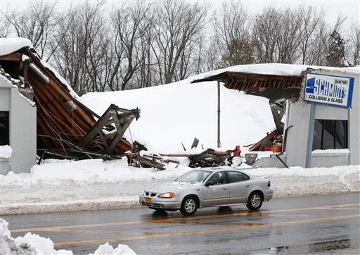 A car drives by Schmidt's Collision and Glass after the roof collapsed after taking on heavy snow during this week's lake-effect snowstorms on Saturday, Nov. 22, 2014, in Hamburg, N.Y. Western New York continues to dig out from the heavy snow dropped by this week by lake-effect snowstorms. (AP Photo/Mike Groll)