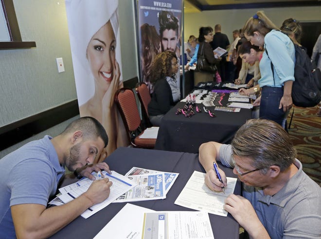 In this Wednesday, Oct. 22, 2014 photo, job seekers Stevens de la Pena, foreground left, and Eduardo Perez, foreground right, fill out a job application at a job fair in Miami Lakes. The number of people seeking U.S. unemployment benefits jumped last week, pushing total applications above 300,000.