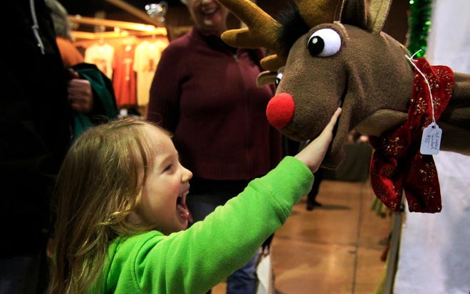 Kira Howe, 4, meets a certain red-nosed reindeer in puppet form Saturday at Holiday Market. She was visiting the market with her grandparents. (The Register-Guard/Paul Carter)