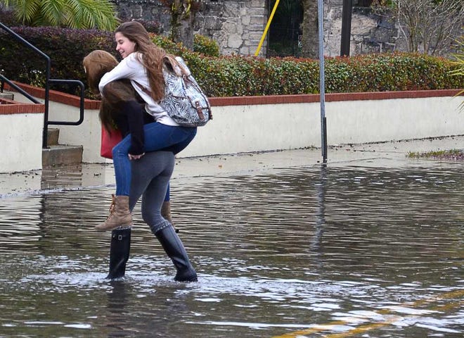 PETER.WILLOTT@STAUGUSTINE.COM Elaina Conklin gives her Flagler College classmate Maria Perez a ride across a flooded Bridge Street in St. Augustine on their way to class on Monday, December 8, 2014. Several streets in St. Augustine flooded Monday because of a high tide and strong winds.