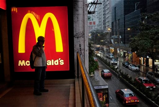 FILE - In this April 2, 2014, file photo, a man talks on a mobile phone next to a downtown McDonald's in Hong Kong. McDonald's says a key global sales figure fell 2.2 percent in November 2014 as U.S. sales continue to soften and it contends with ongoing difficulties from a food-safety scandal in China. (AP Photo/Vincent Yu, File)
